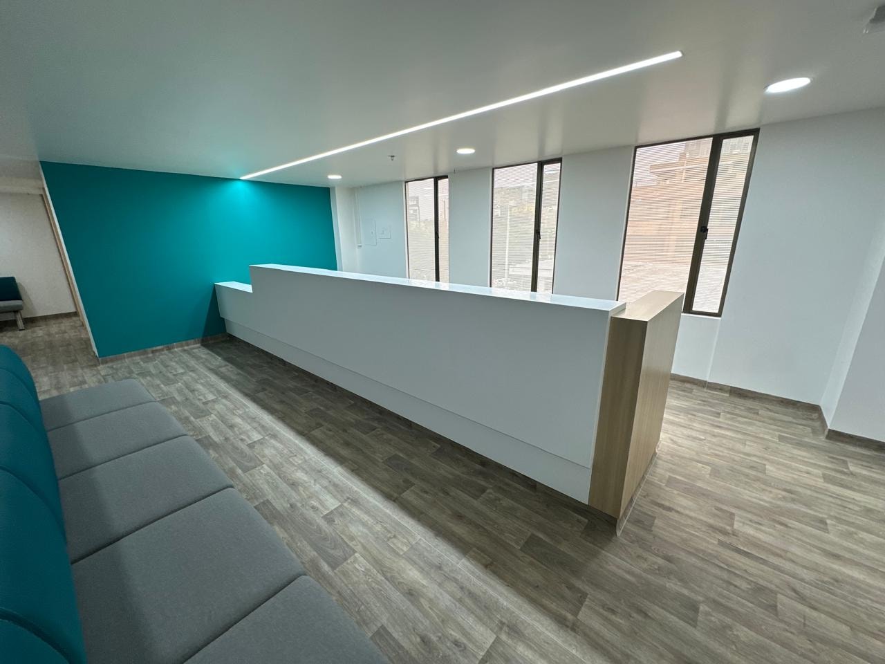 Sala de espera amplia con sillas en verde petróleo, pared de acento teal y señalización de salida