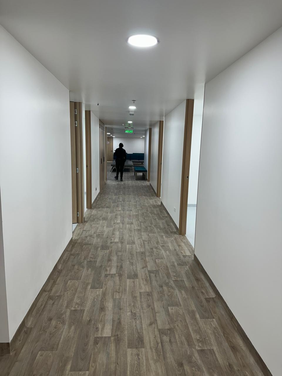 Pasillo de circulación con puertas en madera, piso vinílico y señalización de salida