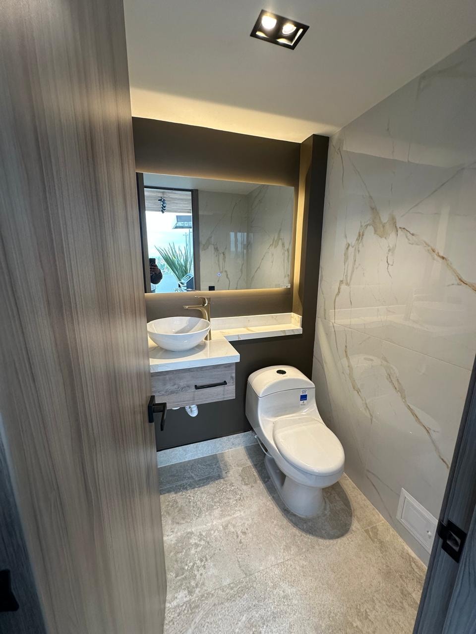 Baño social con mármol blanco, espejo retroiluminado y lavamanos sobre mesón