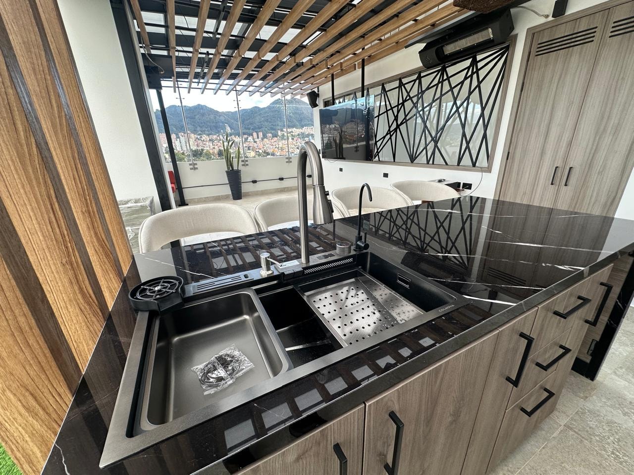Cocina exterior con mesón en mármol negro, fregadero de acero y vista a la terraza