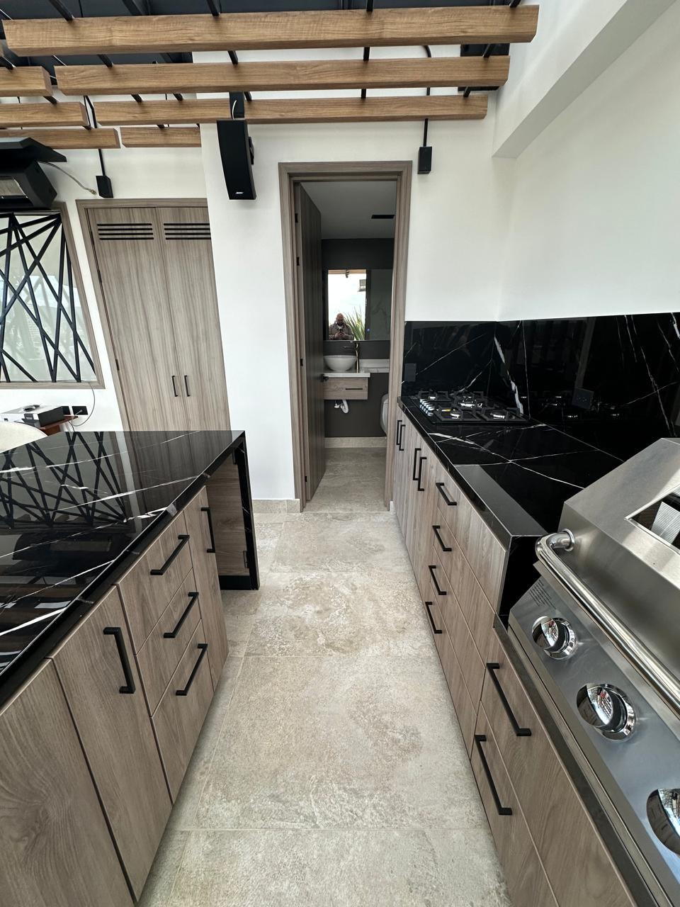 Pasillo de cocina con gabinetes en madera, mármol negro y parrilla de acero inoxidable